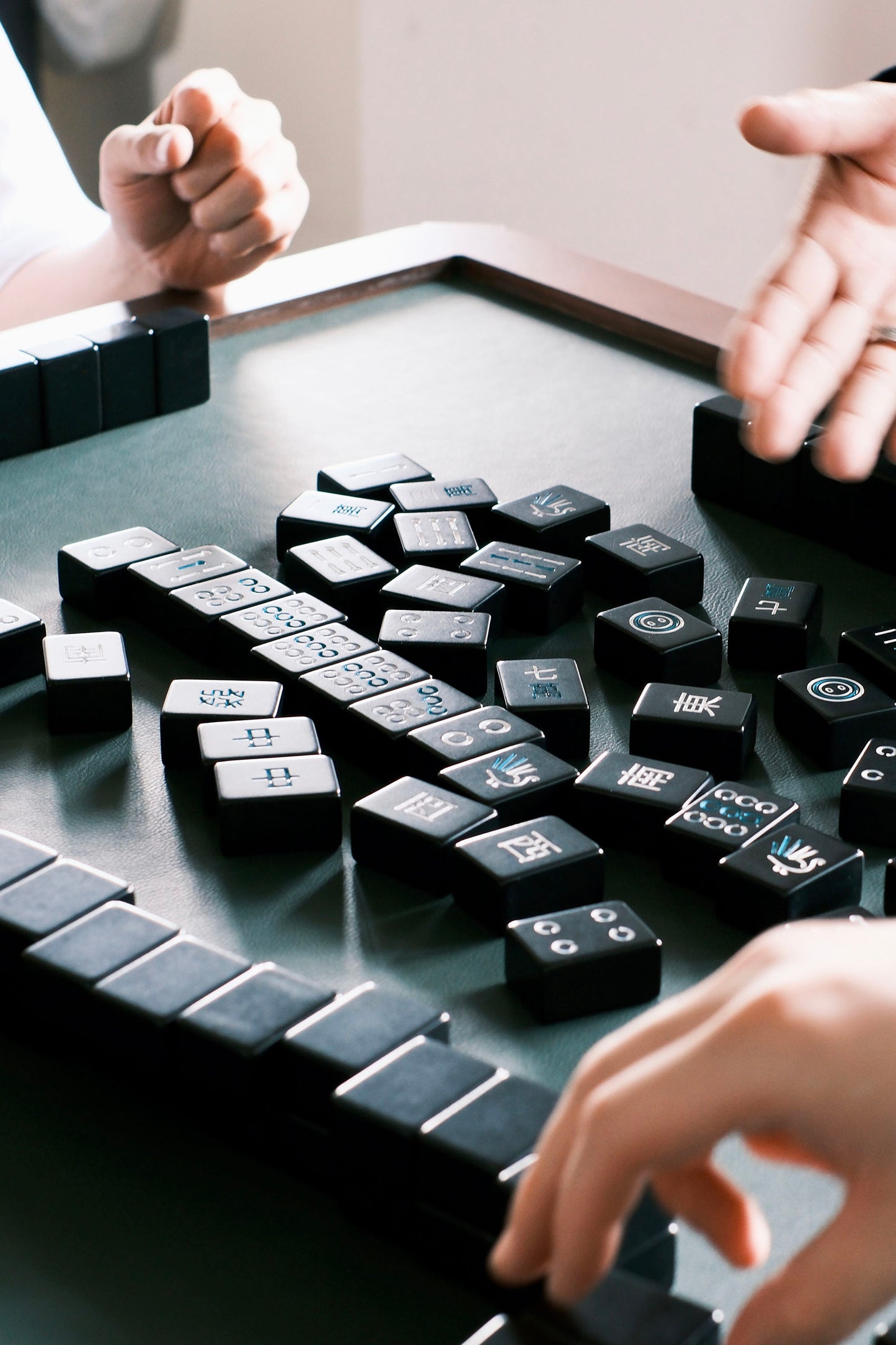 MJ88 Foldable Mahjong Dining Table – close-up of players’ hands and scattered black Mahjong tiles on green felt during gameplay 麻雀餐桌,日本製,對局過程中玩家雙手與散落的黑色麻雀牌特寫,綠色桌面增添真實感。