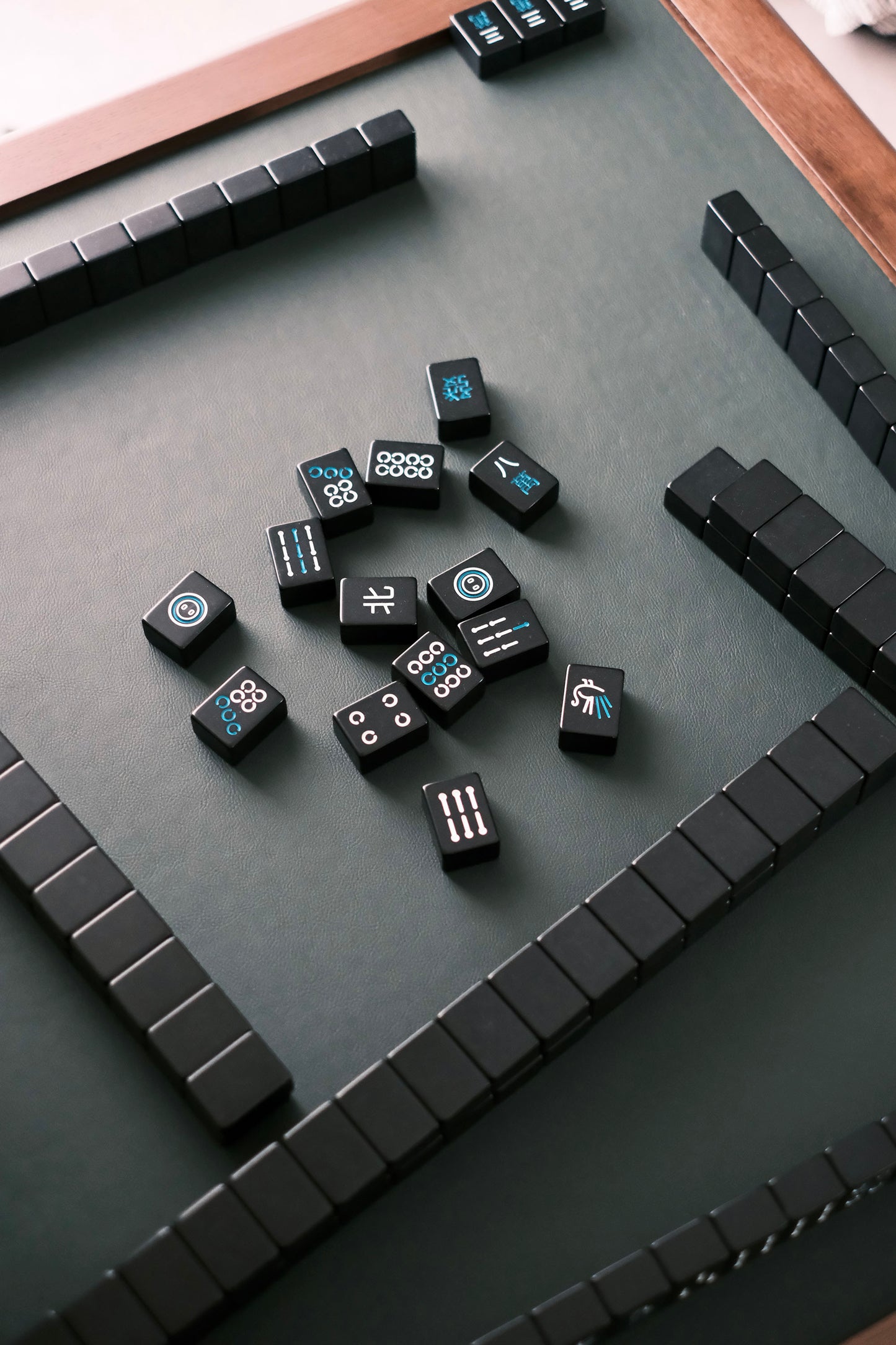 MJ88 Foldable Mahjong Dining Table – overhead view of black Mahjong tiles with elegant white and blue patterns on green leather surface 麻雀餐桌,日本製,從上方俯視黑色麻雀牌,牌面以白藍色圖紋點綴,搭配深綠色人造皮革枱面。