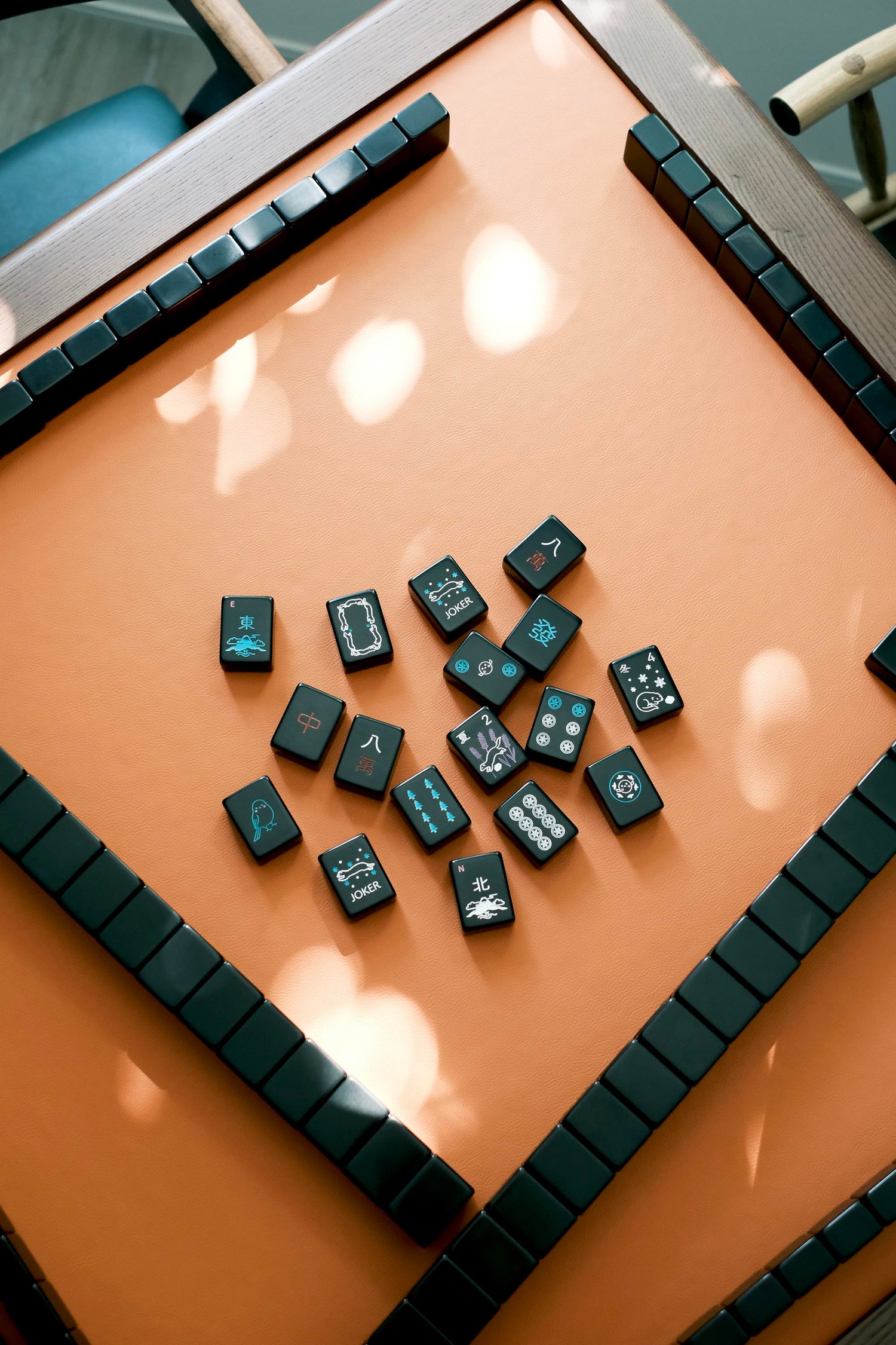 Black Hokkaido-theme mahjong tiles scattered across the corner of the leather playing surface
黑色北海道主題麻雀牌散落於皮革桌面一角