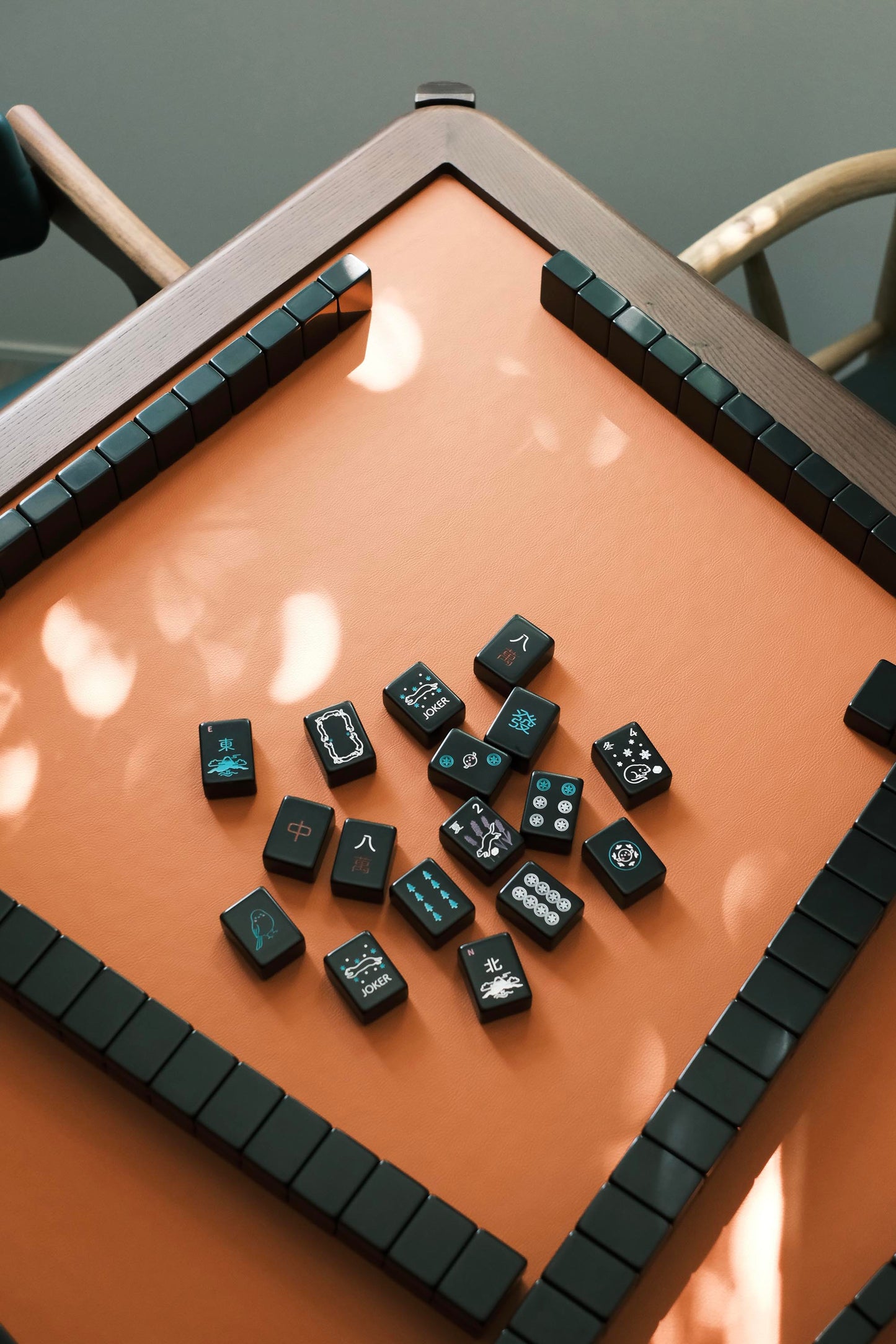 Black mahjong tiles with hand-drawn Hokkaido motifs scattered on the MJ88R leather playing surface
黑色麻雀牌散落 MJ88R 皮革桌面，牌面為手繪北海道圖案