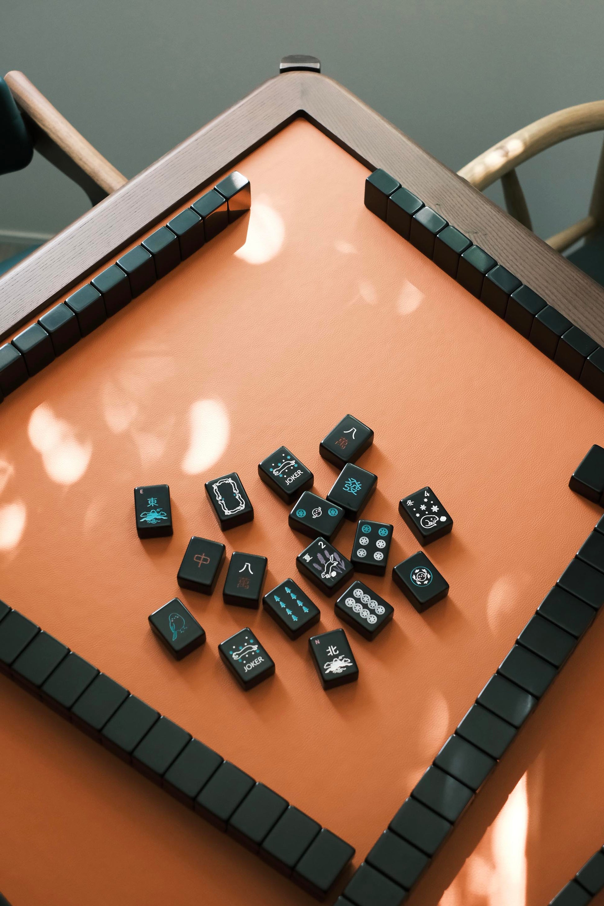 Black mahjong tiles with hand-drawn Hokkaido motifs scattered on the MJ88R leather playing surface
黑色麻雀牌散落 MJ88R 皮革桌面，牌面為手繪北海道圖案