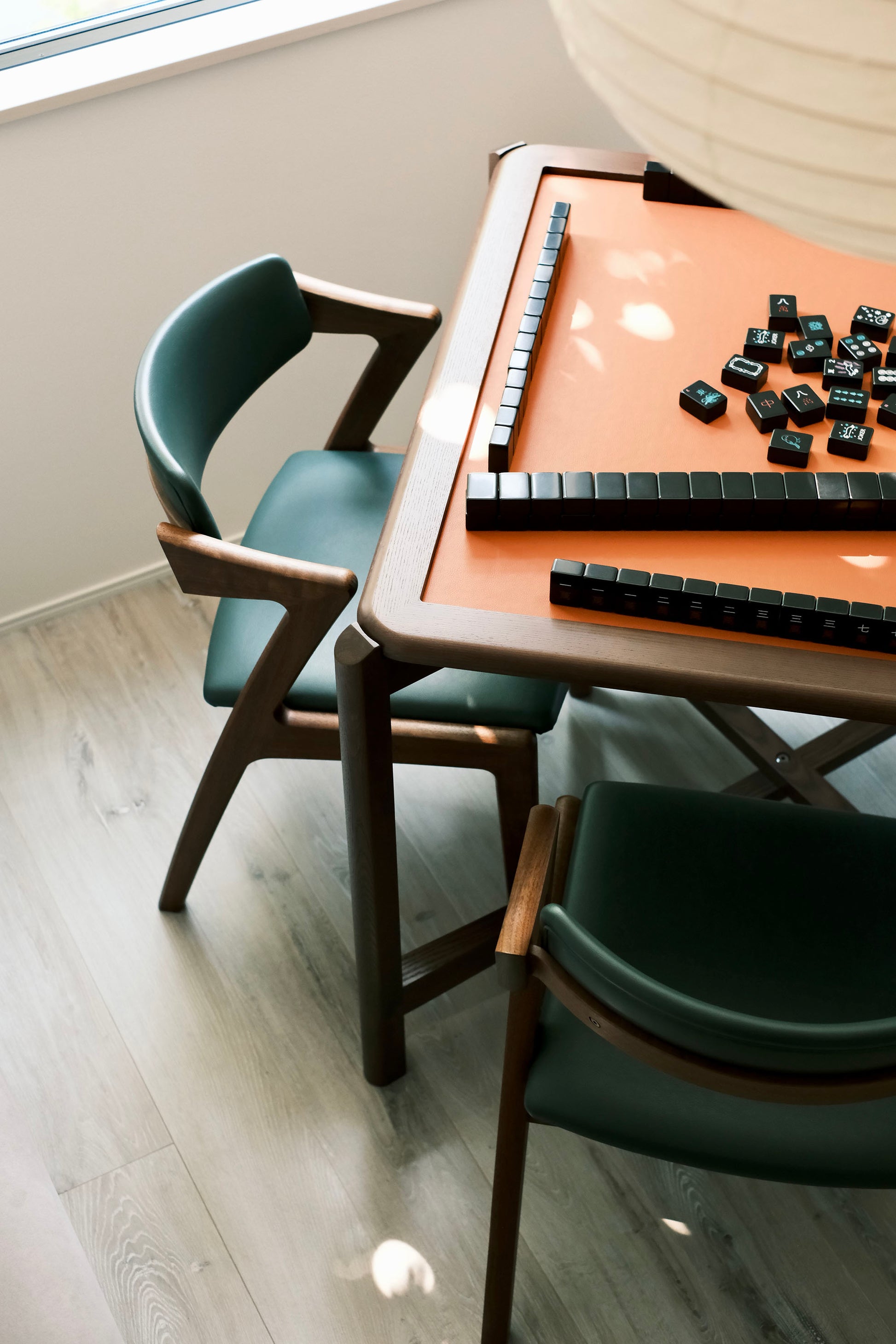 MJ88R foldable mahjong dining table set by a window with green chairs and black tiles laid out
MJ88R 摺疊麻雀餐桌置於窗邊，配綠色餐椅與已排好的黑色麻雀牌